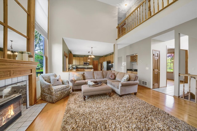 living room featuring a tiled fireplace, a healthy amount of sunlight, light wood-type flooring, and a towering ceiling