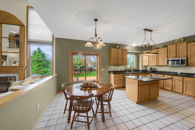 kitchen featuring light tile patterned floors, a tile fireplace, appliances with stainless steel finishes, dark countertops, and a notable chandelier