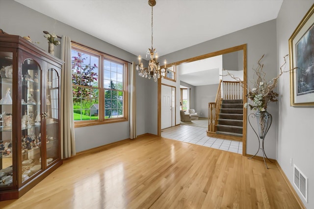 unfurnished dining area with visible vents, baseboards, stairs, an inviting chandelier, and wood finished floors