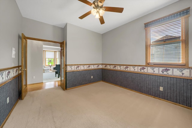 carpeted empty room with ceiling fan, wainscoting, and wallpapered walls