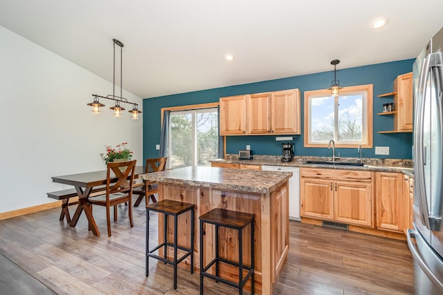 kitchen featuring white dishwasher, a sink, vaulted ceiling, light wood-style floors, and a center island