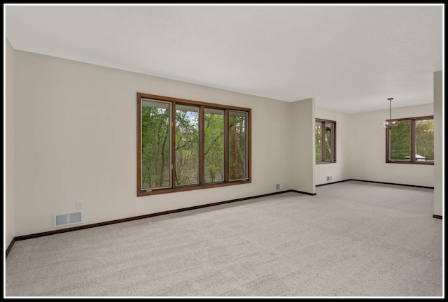 carpeted empty room featuring a notable chandelier, baseboards, and visible vents