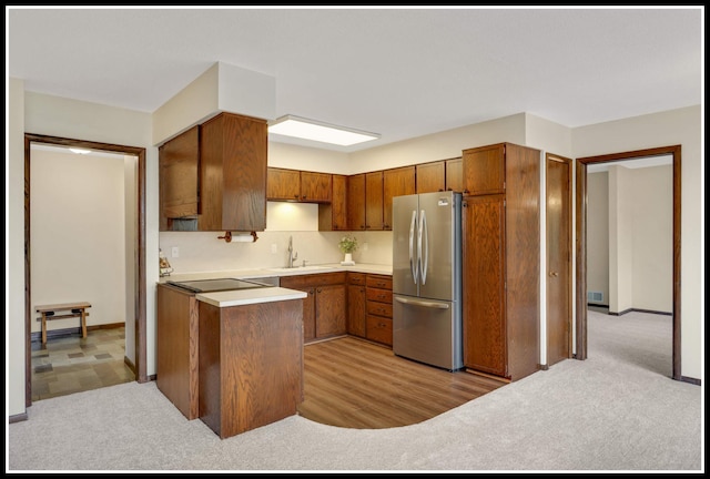 kitchen featuring a sink, freestanding refrigerator, brown cabinetry, light countertops, and light carpet