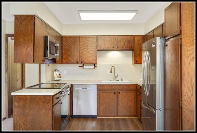 kitchen with a sink, brown cabinetry, light countertops, and appliances with stainless steel finishes