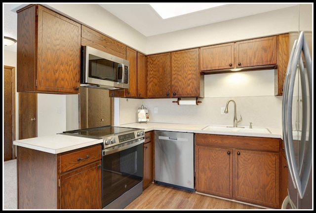 kitchen featuring stainless steel appliances, a sink, brown cabinets, light countertops, and light wood-type flooring