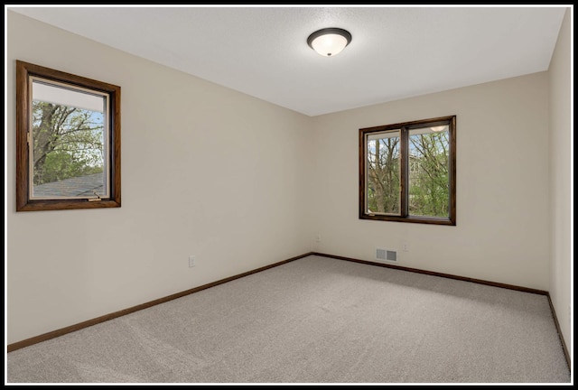 empty room with baseboards, carpet flooring, visible vents, and plenty of natural light