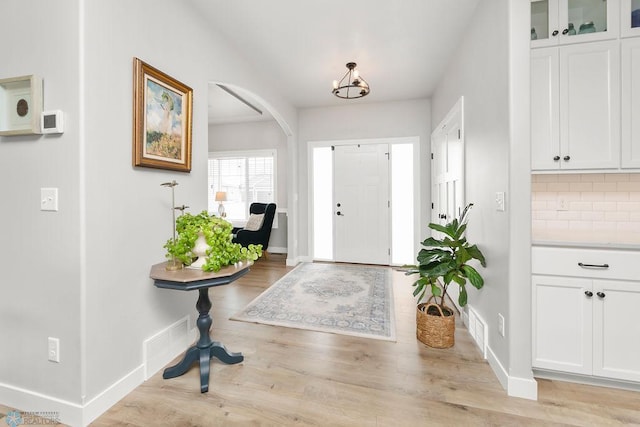 foyer with light wood-type flooring, arched walkways, and baseboards