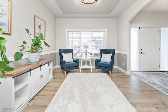 living area with a tray ceiling, arched walkways, baseboards, and light wood finished floors