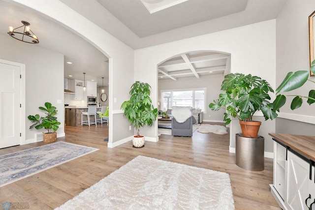 entryway with arched walkways, light wood-style flooring, coffered ceiling, and baseboards