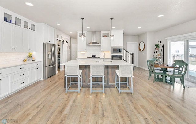 kitchen with light wood finished floors, a breakfast bar, light countertops, stainless steel appliances, and wall chimney exhaust hood