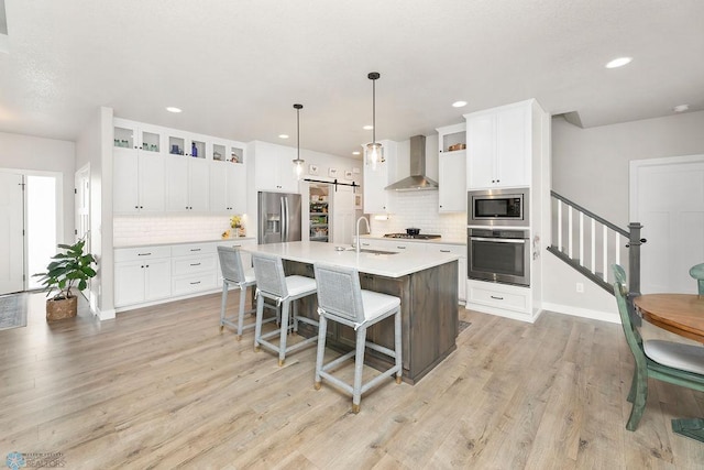 kitchen featuring light wood-type flooring, stainless steel appliances, a barn door, a breakfast bar area, and wall chimney exhaust hood