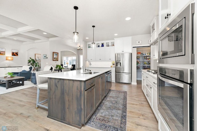 kitchen with light wood finished floors, light countertops, appliances with stainless steel finishes, white cabinetry, and a sink