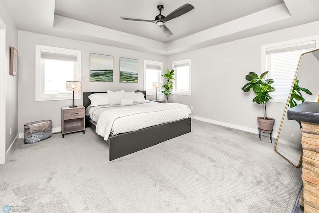 carpeted bedroom featuring baseboards, a raised ceiling, and a ceiling fan