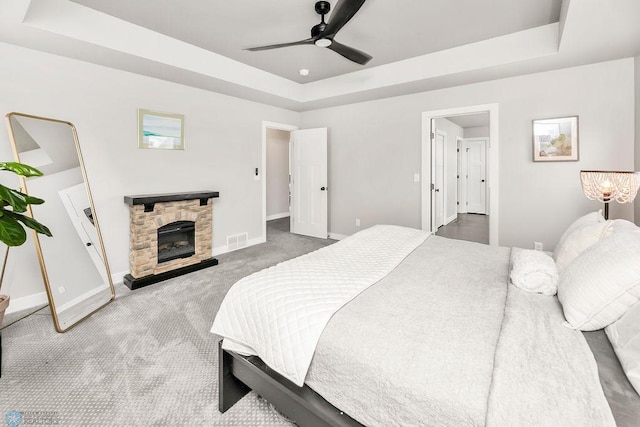 carpeted bedroom with a tray ceiling, baseboards, visible vents, and a fireplace