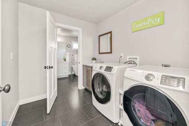 washroom featuring baseboards, cabinet space, a sink, washer and dryer, and dark tile patterned floors