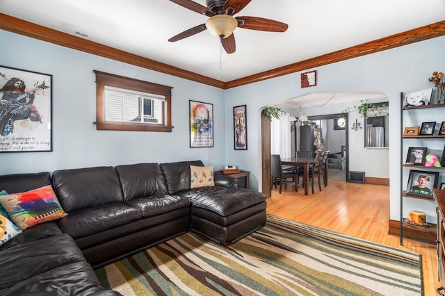 living area featuring ornamental molding, wood finished floors, arched walkways, and ceiling fan