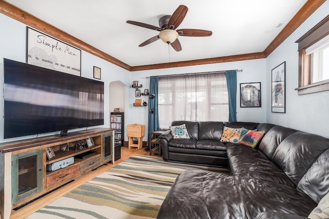 living area featuring arched walkways, wood finished floors, a ceiling fan, and crown molding