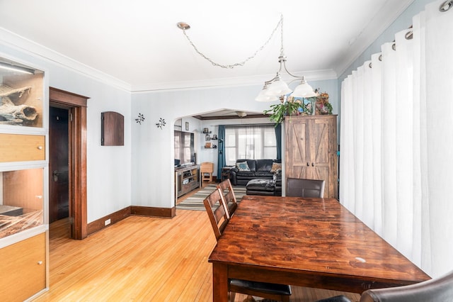 dining room with crown molding, light wood-style flooring, baseboards, and arched walkways