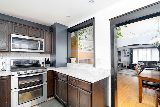 kitchen with decorative backsplash, dark brown cabinets, stainless steel appliances, and light countertops