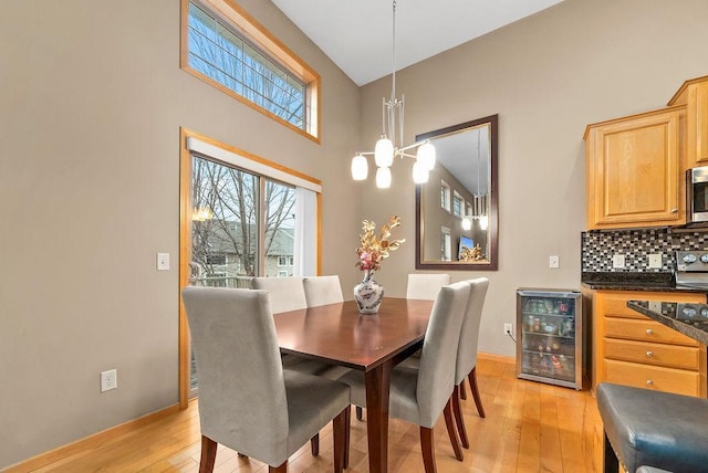 dining space featuring wine cooler, an inviting chandelier, baseboards, and light wood-style floors