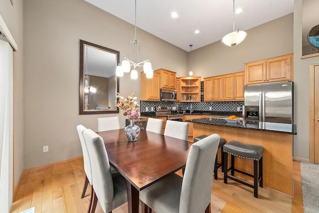 dining area featuring a high ceiling, light wood-style floors, baseboards, and a chandelier