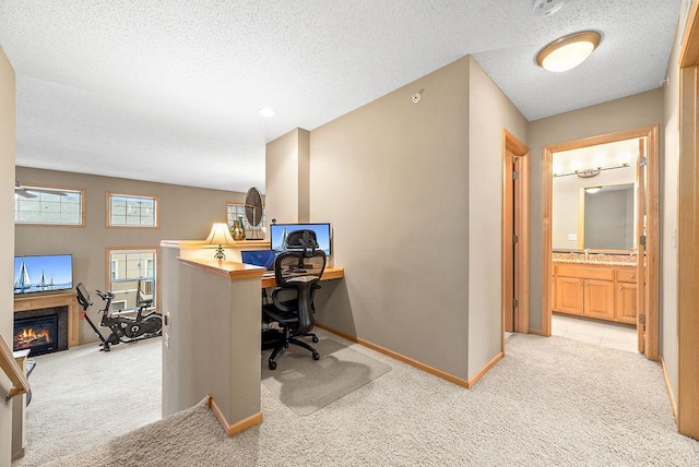 office space with baseboards, light carpet, a glass covered fireplace, a textured ceiling, and a ceiling fan