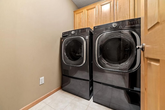 washroom with a textured ceiling, cabinet space, separate washer and dryer, light tile patterned floors, and baseboards