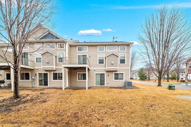 rear view of house featuring a balcony, central air condition unit, and a yard