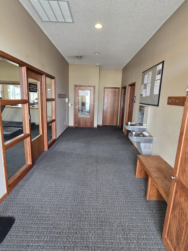 corridor with lofted ceiling, dark carpet, and a textured ceiling