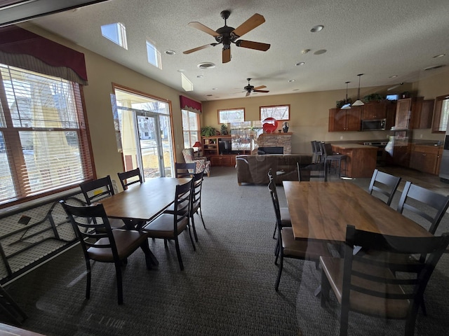 dining space featuring a fireplace, a ceiling fan, dark carpet, and a textured ceiling