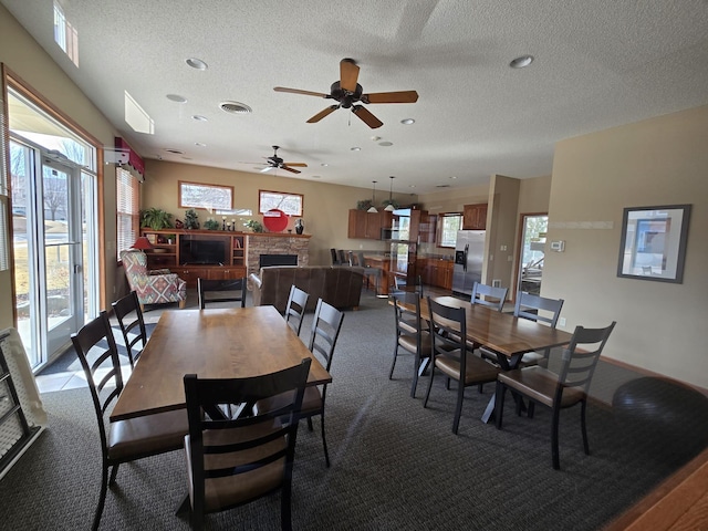 carpeted dining area featuring visible vents, a fireplace, a textured ceiling, and a ceiling fan