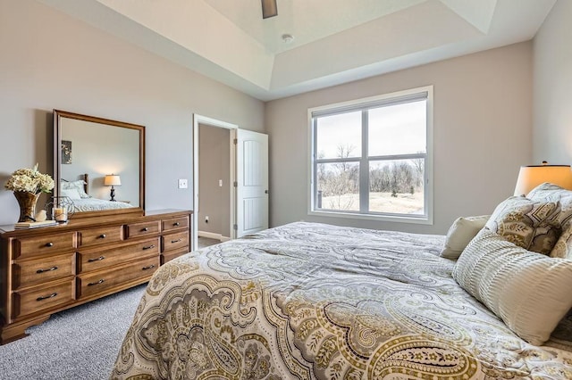 carpeted bedroom featuring a raised ceiling and a ceiling fan