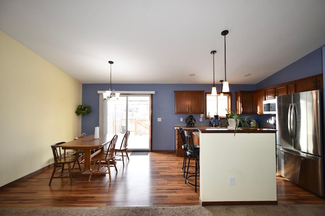 kitchen with dark wood-type flooring, a kitchen breakfast bar, appliances with stainless steel finishes, a chandelier, and vaulted ceiling