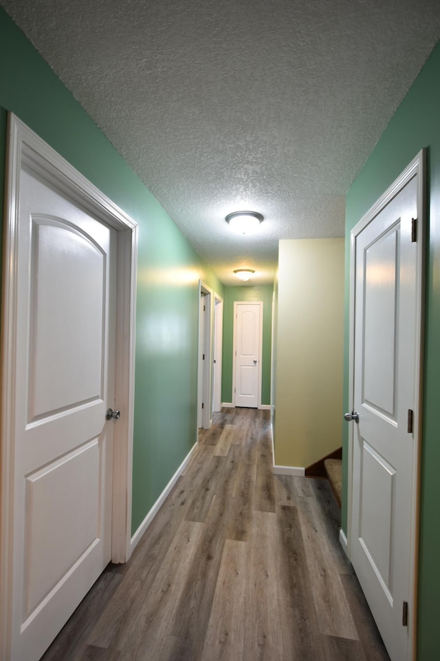 hallway with baseboards, a textured ceiling, and wood finished floors