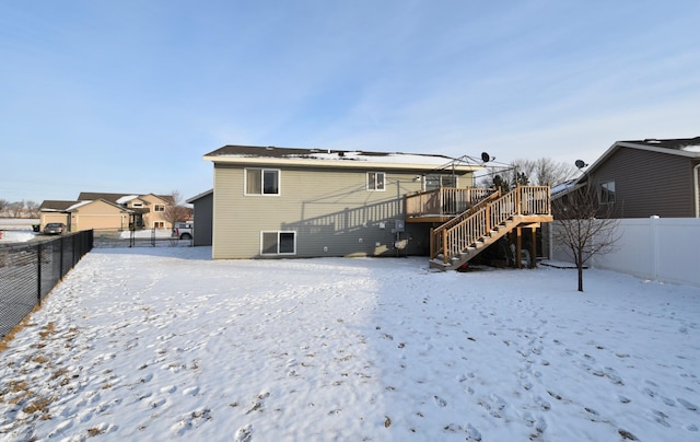 snow covered back of property with stairway, a wooden deck, and a fenced backyard