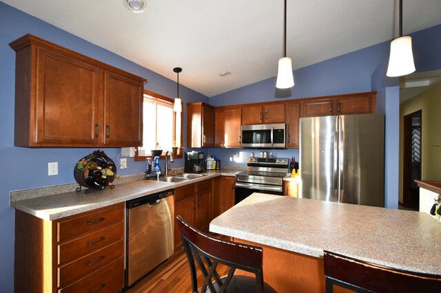 kitchen with pendant lighting, vaulted ceiling, appliances with stainless steel finishes, wood finished floors, and a sink