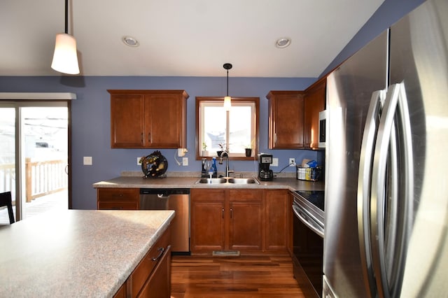 kitchen featuring brown cabinets, pendant lighting, a sink, dark wood finished floors, and appliances with stainless steel finishes