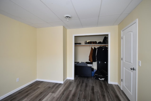 bedroom with baseboards, wood finished floors, a closet, and a paneled ceiling