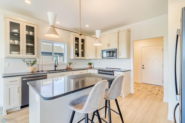 kitchen with light wood-type flooring, a sink, dark countertops, appliances with stainless steel finishes, and a breakfast bar area