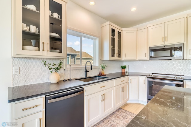 kitchen with decorative backsplash, dark stone countertops, appliances with stainless steel finishes, and a sink