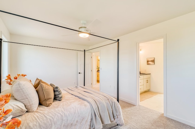 bedroom with ensuite bath, light colored carpet, baseboards, and ceiling fan