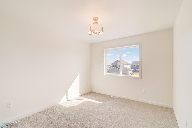 empty room with visible vents, light colored carpet, an inviting chandelier, and baseboards