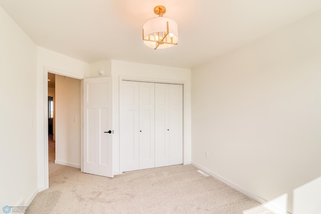 unfurnished bedroom featuring light colored carpet, baseboards, a closet, and a chandelier