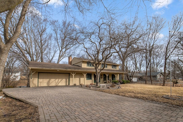 view of front of home featuring decorative driveway, an attached garage, covered porch, and a chimney