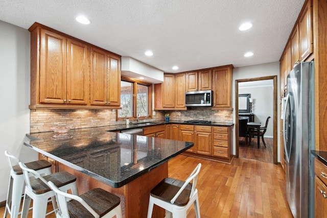 kitchen with brown cabinets, appliances with stainless steel finishes, a kitchen bar, and a peninsula