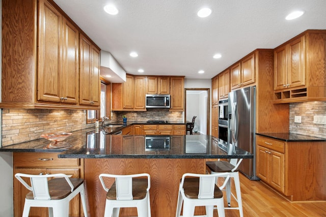 kitchen featuring brown cabinets, a peninsula, stainless steel appliances, and dark stone countertops