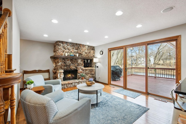 living room featuring light wood-type flooring, visible vents, a textured ceiling, recessed lighting, and a stone fireplace