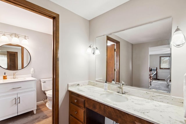 bathroom featuring two vanities, toilet, wood finished floors, and a sink