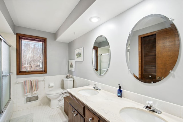 bathroom with tile walls, toilet, tile patterned floors, and a sink