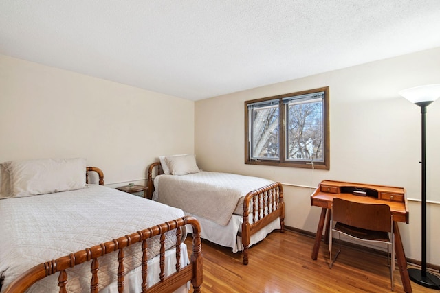 bedroom featuring baseboards, light wood-type flooring, and a textured ceiling